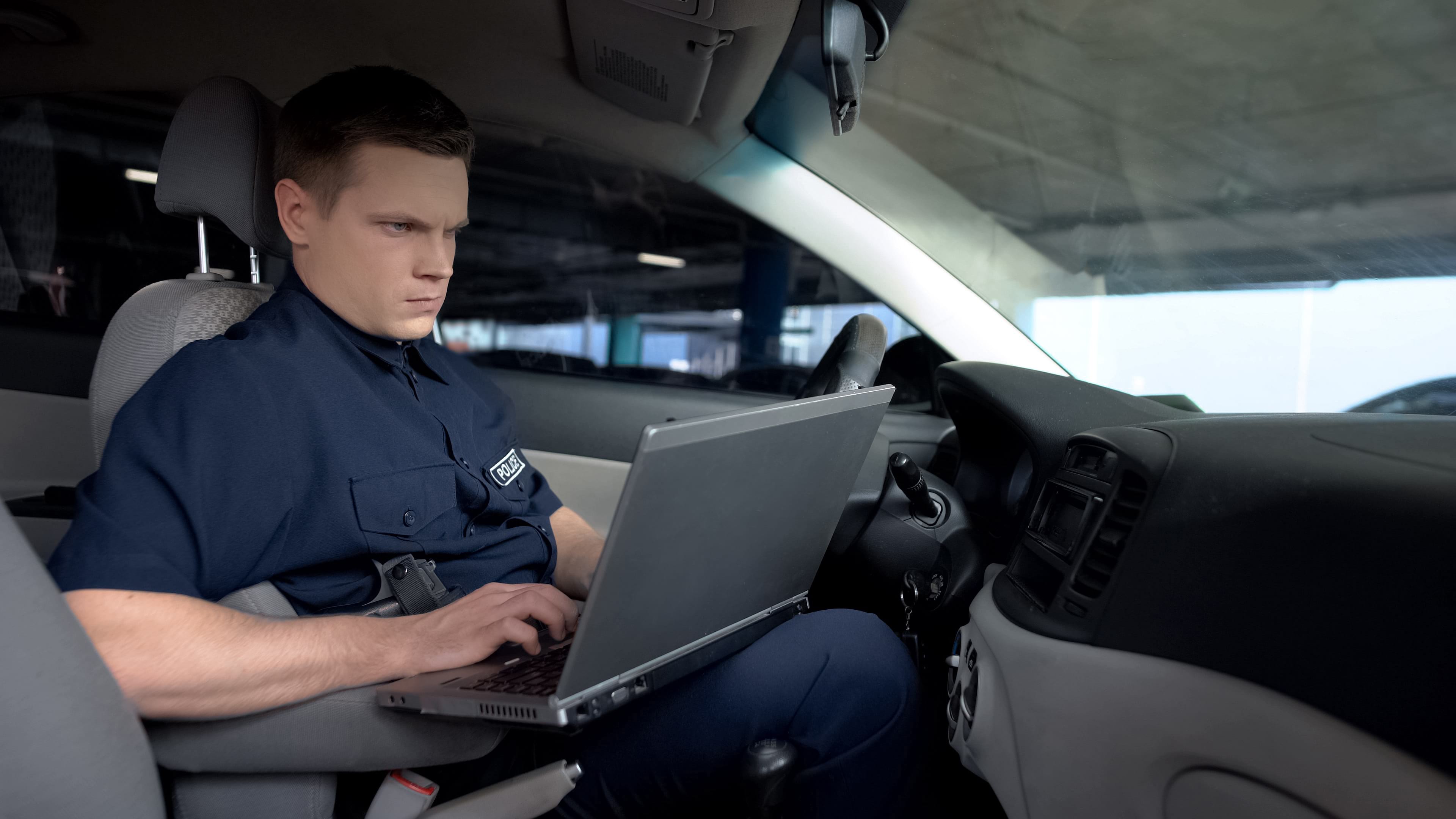 Police officer in patrol car with laptop